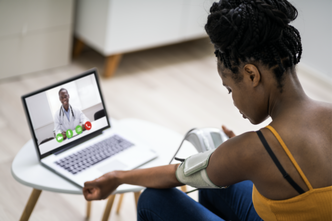 Young woman taking her own blood pressure while speaking to a medical professional over a video call.