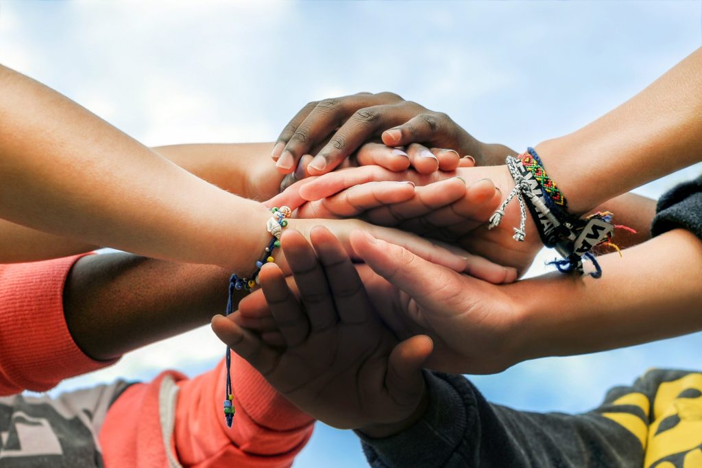 A group of hands piled on top of each other ranging in skin tone to indicate diversity.